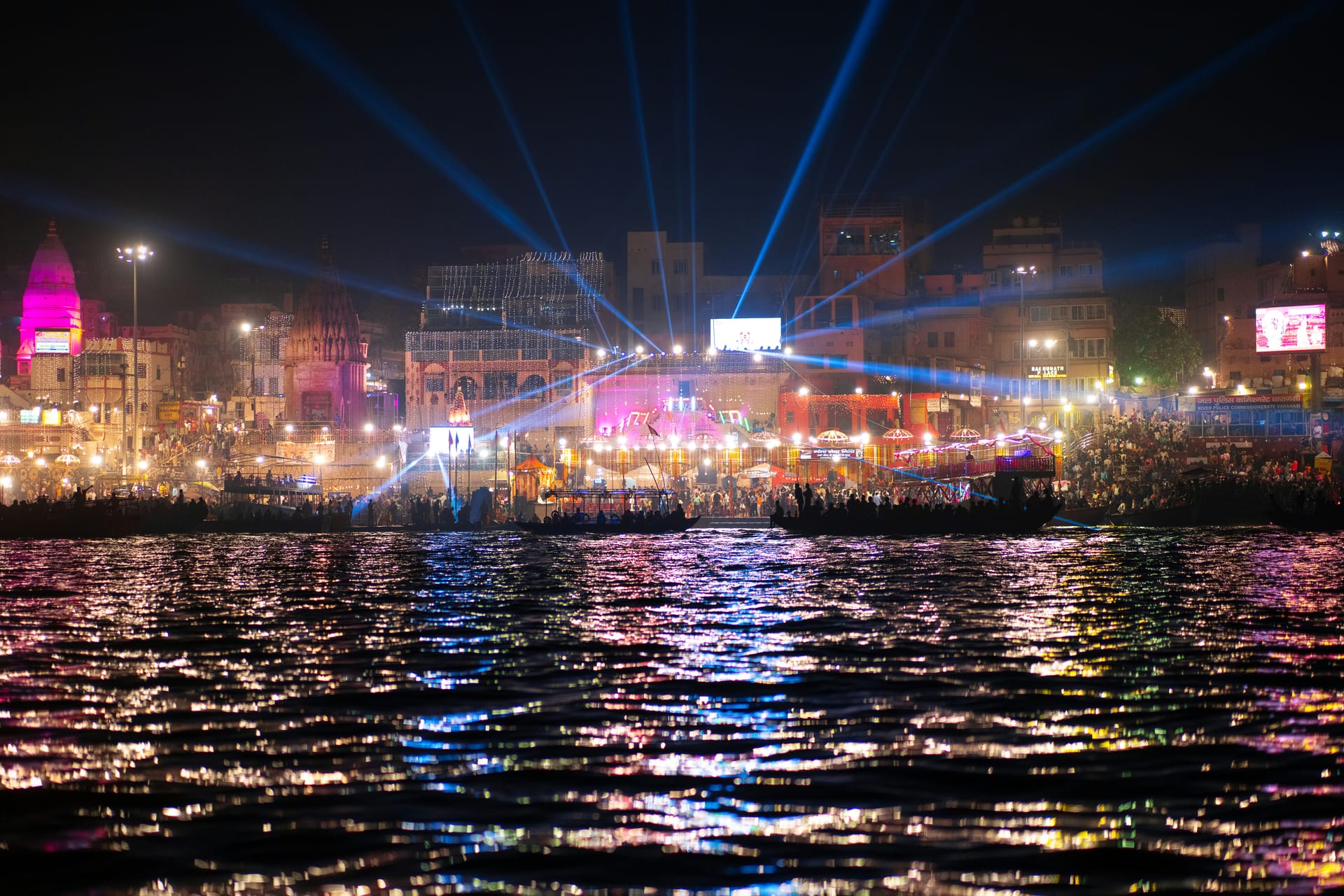 Evening aarti ceremony at the ghats of Varanasi with flickering lamps, pilgrims bathing in the Ganges, and boats on the river